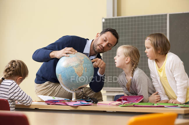 Teacher and pupils looking at globe in classroom — Stock Photo