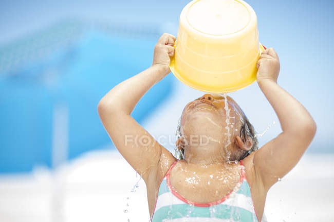 Chica salpicándose con un cubo de agua en la playa - foto de stock