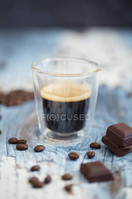 Coupe en verre d'espresso, grains de café torréfiés et chocolat noir sur bois — Photo de stock
