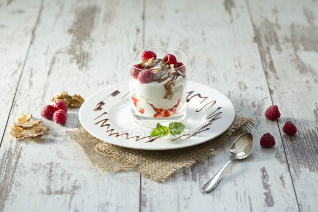 Dessert in glass with raspberries, curd, yoghurt, dried apple, almond slivers and chocolate sauce — Stock Photo