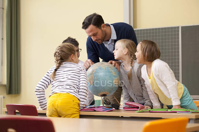 Profesores y alumnos mirando el globo en el aula - foto de stock