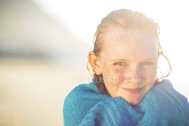 Portrait of smiling girl on the beach wrapped in a beach towel — Stock Photo