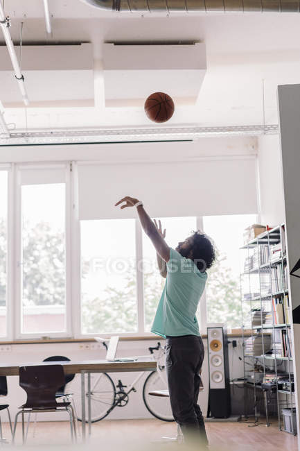 Young man playing with basketball in office — Stock Photo