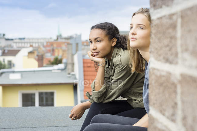 Две девочки-подростки сидят на крыше и смотрят на расстояние — стоковое фото