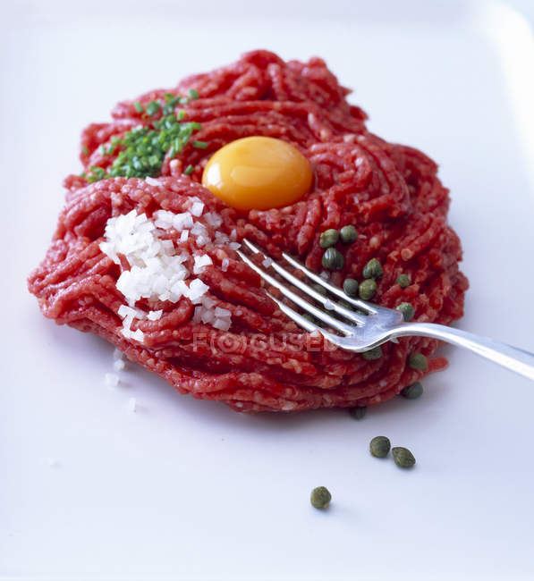 Raw steak tatar with egg yolk, diced onion, capers and chives — Stock Photo