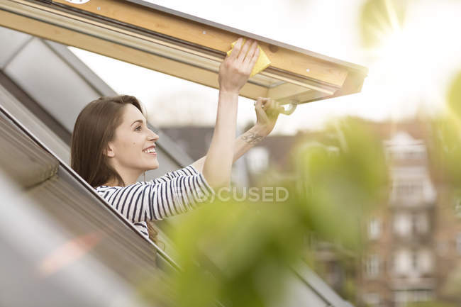 Sonriente joven mujer limpiando la ventana del techo — Stock Photo