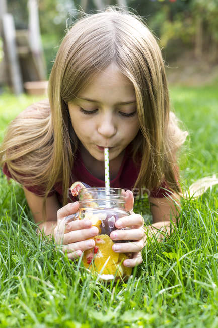 Mädchen liegt auf einer Wiese und trinkt Wasser mit verschiedenen Früchten — Stockfoto