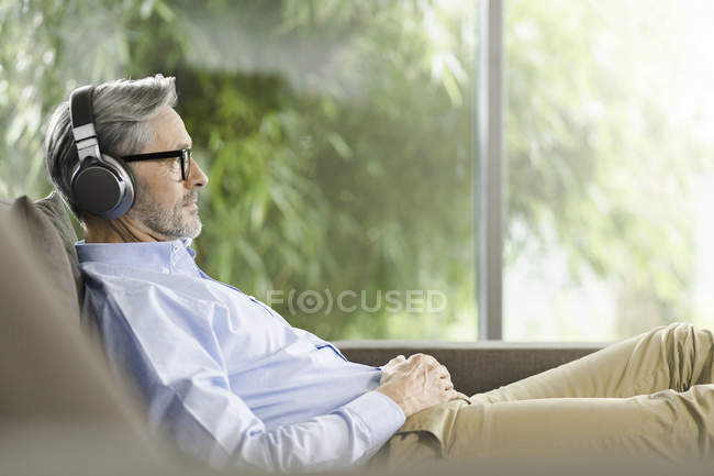 Homem relaxante no sofá ouvindo música com fones de ouvido — Fotografia de Stock