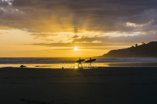 Silhouettes of two people with surfboards on the beach at twilight — Stock Photo