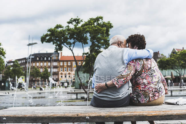 Back view of kissing senior couple sitting on a bench hugging each other — Stock Photo