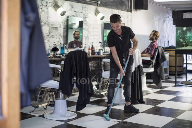 Friseur fegt Haare im Friseursalon auf dem Fußboden — Stockfoto