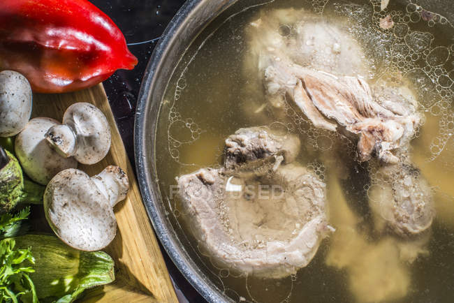 М'ясо в кухонному горщику і дерев'яний стіл з овочами — стокове фото