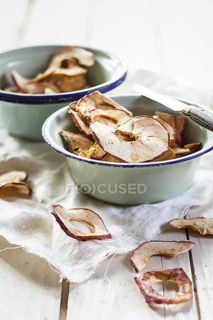 Patatas fritas de manzana orgánica en cuencos sobre mesa de madera con paño - foto de stock