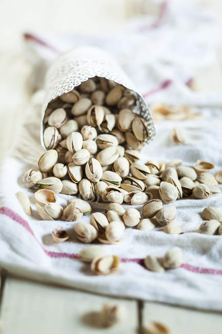 Cup of roasted and salted pistachios on kitchen towel — Stock Photo