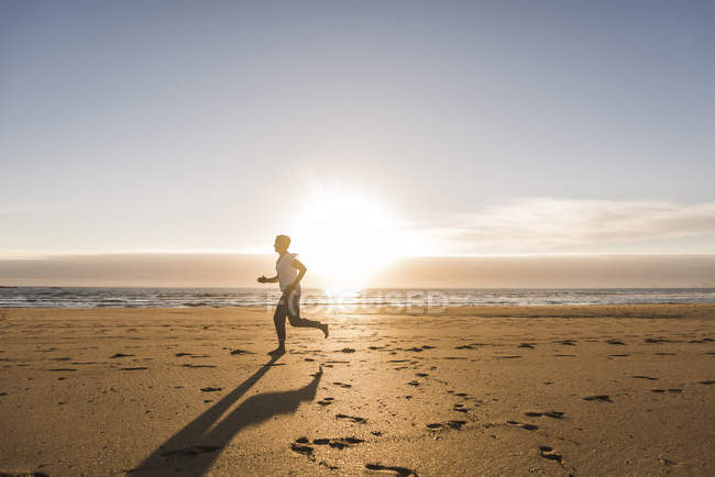 Mujer corriendo en la playa de arena al atardecer - foto de stock