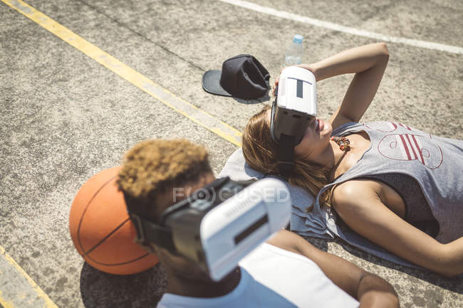 Jeune couple utilisant des lunettes de réalité virtuelle, les têtes reposées sur le basket — Photo de stock