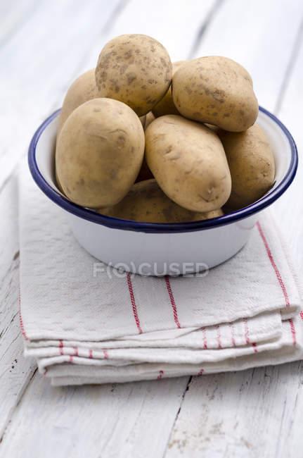 Bowl of raw potatoes on folded kitchen towel and wood — Stock Photo