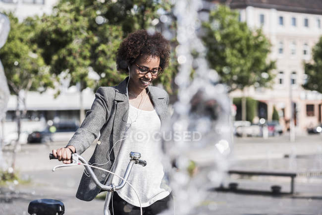Retrato de mujer sonriente con bicicleta escuchando música con auriculares - foto de stock
