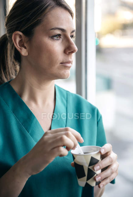 Mujer en uniforme tomando un descanso para tomar café mirando por la ventana - foto de stock