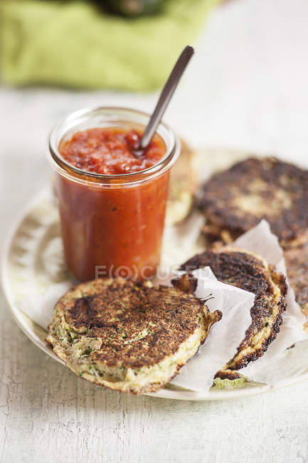 Dish of zucchini fritters and glass of tomato sauce — Stock Photo