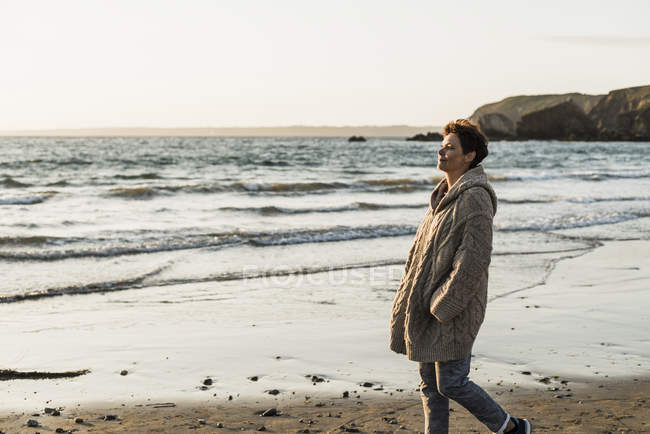 Francia, penisola di Crozon, donna in cardigan che cammina sulla spiaggia al tramonto — Foto stock
