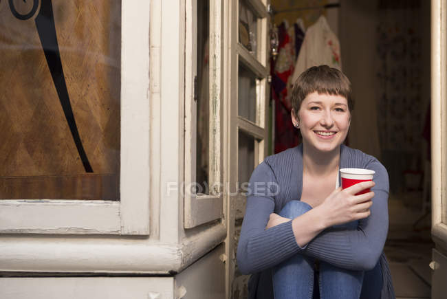 Портрет женщины-модельера с чашкой кофе, сидящей у входа в студию — стоковое фото