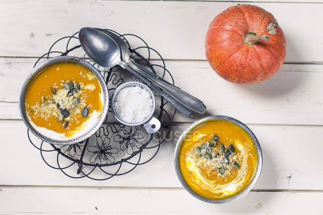 Two bowls of Exotic pumpkin soup with coconut milk and coconut flakes, spoons and pumpkin on white wood — Stock Photo