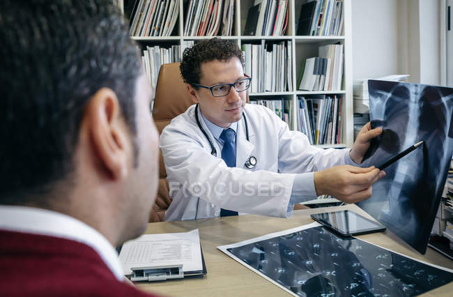 Врач показывает рентгеновское изображение пациенту в медицинском кабинете — стоковое фото