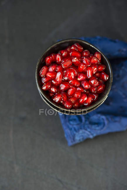 Metal bowls of pomegranate seeds on blue cloth and grey ground — Stock Photo
