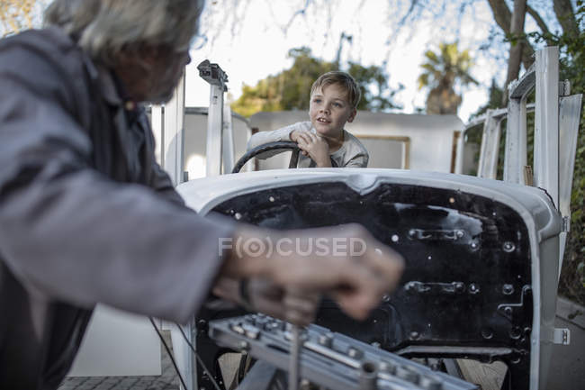 Старший мужчина восстанавливает винтажную машину с парнем, сидящим внутри — стоковое фото