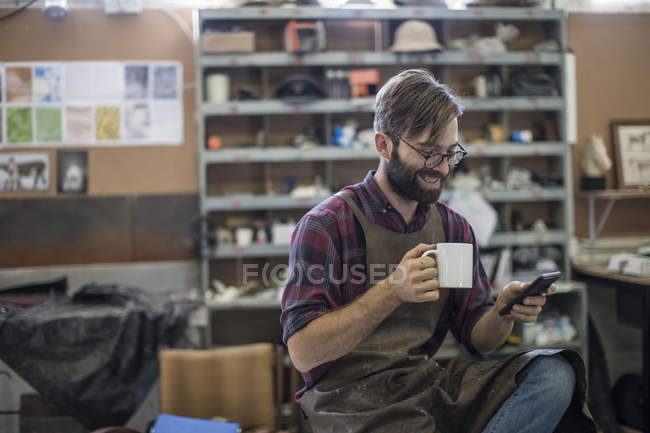 Homme avec téléphone portable ayant une pause café dans l'atelier — Photo de stock