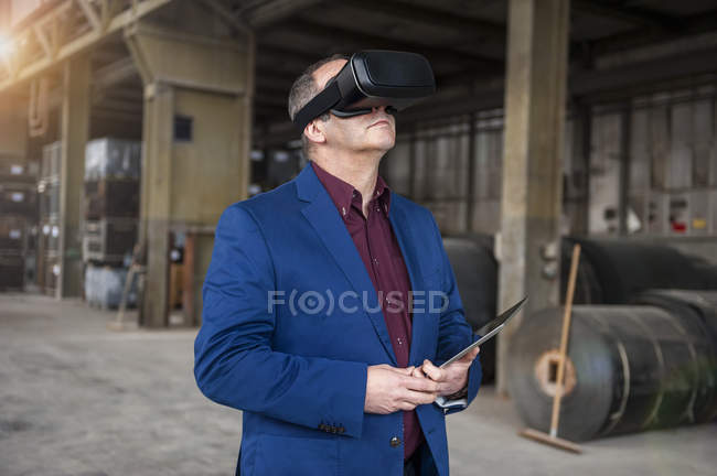 Manager standing in factory hall looking through VR glasses — Stock Photo