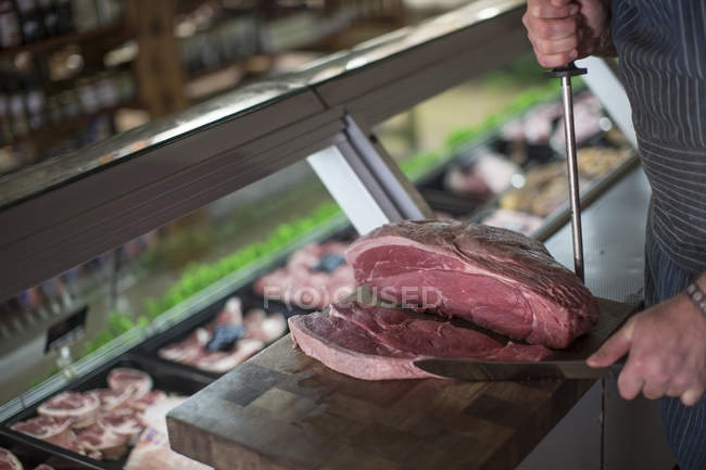 Butcher cutting raw steak on wooden board — Stock Photo