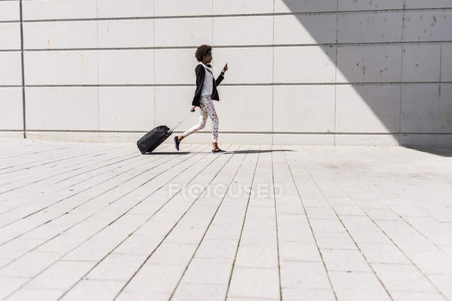 Camminando donna d'affari con trolley bag guardando il suo smartphone — Foto stock