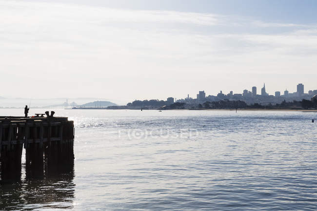 EE.UU., California, San Francisco skyline y pescador en el muelle - foto de stock