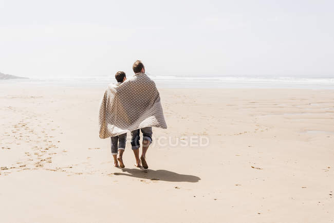 Coppia matura passeggiando sulla spiaggia con coperta — Foto stock