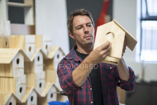 Homem segurando casa de pássaros inacabada na oficina — Fotografia de Stock