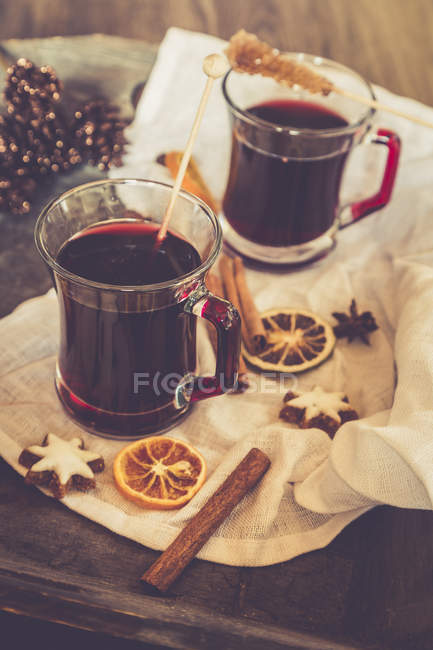 Verres de vin chaud, tranches d'orange et étoiles de cannelle sur tissu et plateau en bois — Photo de stock