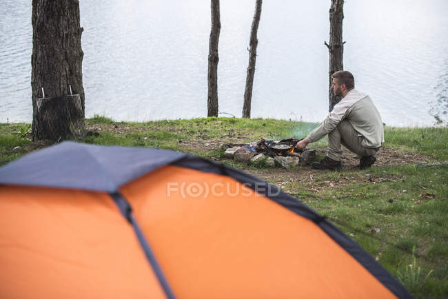 L'uomo che frigge a fuoco di campo a riva di un lago — Foto stock
