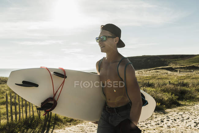 Giovane uomo che trasporta la tavola da surf sulla costa — Foto stock