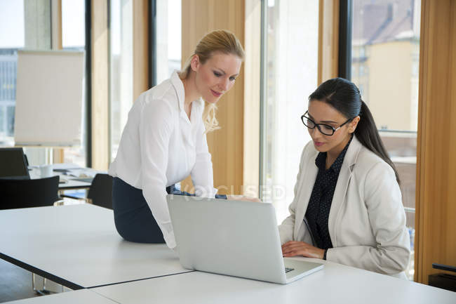 Two businesswomen in office working together on laptop — meeting ...