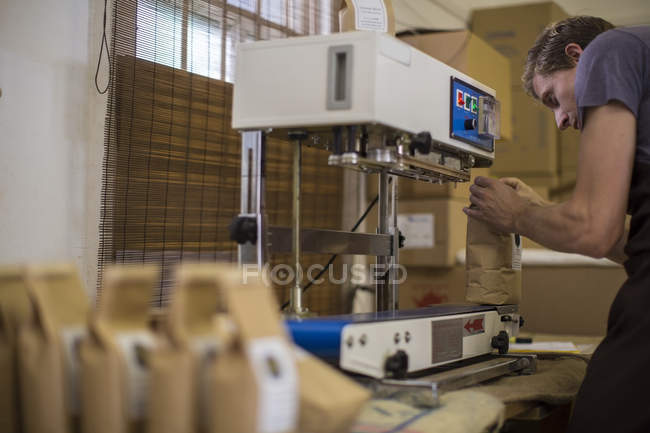 Uomo che lavora al confezionamento del chicco di caffè sottovuoto sigillante — Foto stock