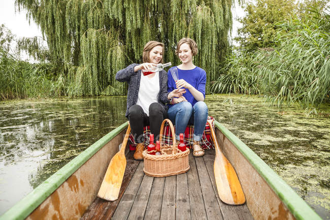 Deux jeunes femmes en bateau à rames avec bouteille et verre — Photo de stock