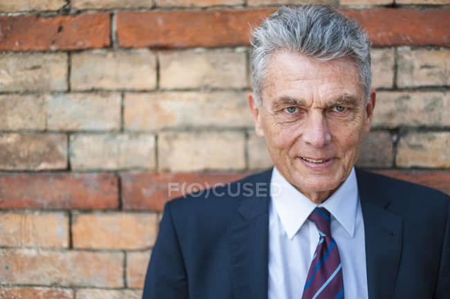 Ritratto di uomo d'affari anziano fiducioso al muro di mattoni — Foto stock