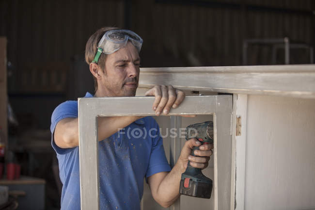 Carpintero usando un taladro inalámbrico en un gabinete - foto de stock