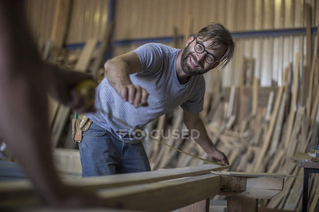 Falegname sorridente misura tagliere in legno in officina — Foto stock