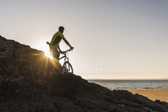 Francia, península de Crozon, ciclista de montaña mirando el atardecer - foto de stock