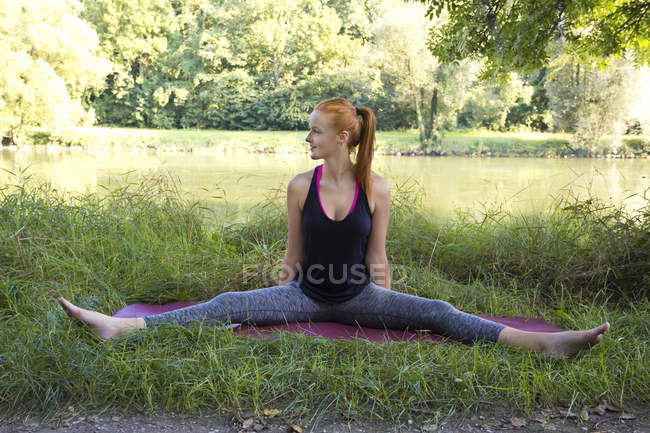 Mujer joven estirándose en la alfombra de gimnasio en un prado - foto de stock
