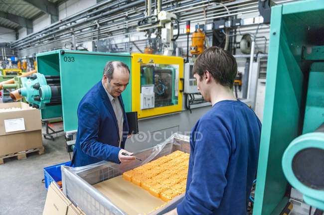 Gerente e trabalhador examinando produtos plásticos na fábrica — Fotografia de Stock