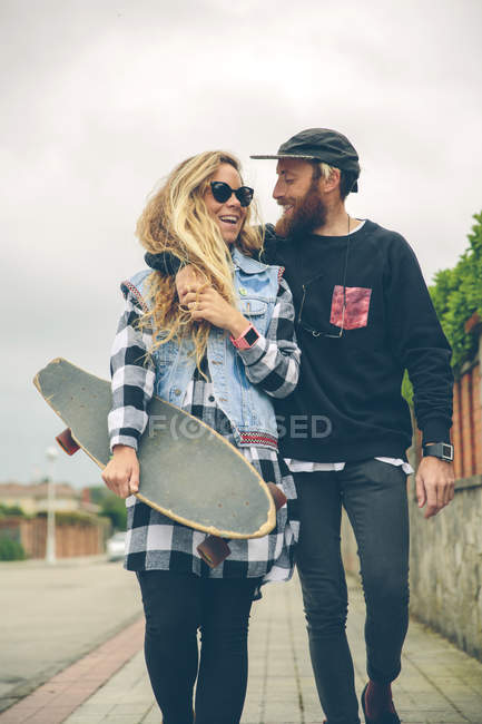 Happy couple with skateboard walking on pavement — Stock Photo